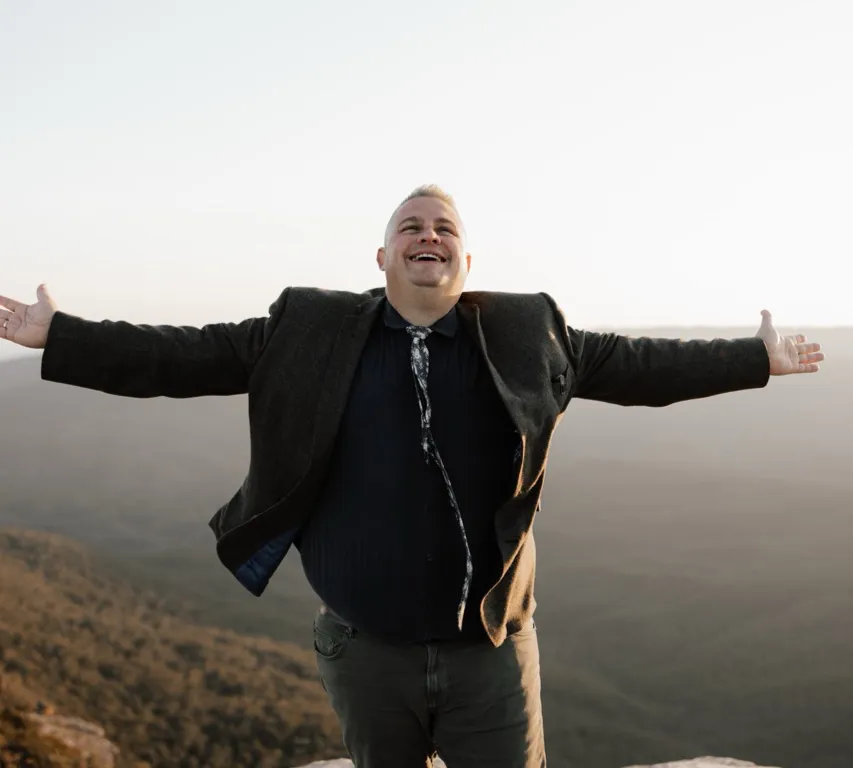 Josh with arms outstretched, laughing in the late afternoon sun.